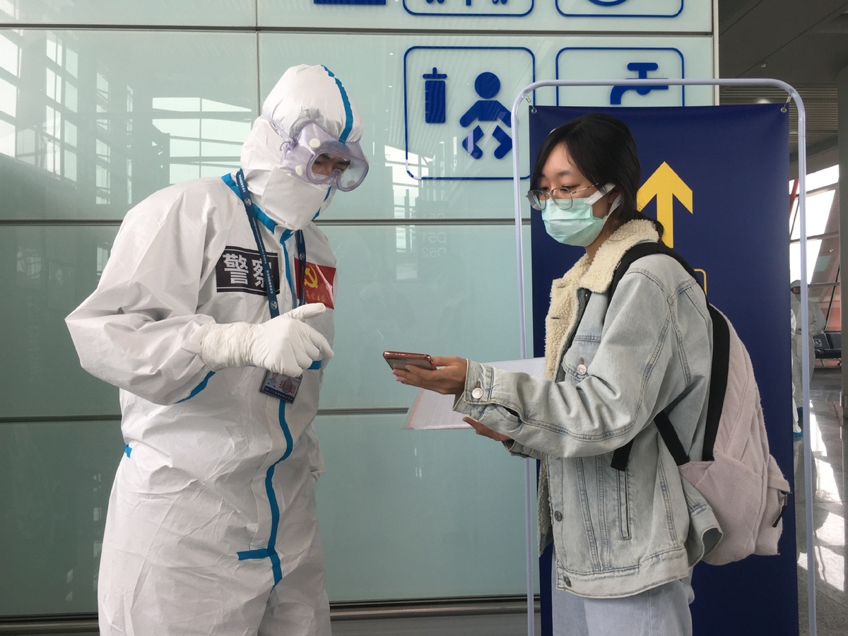 Staff in protective suits talks with a passenger at the Beijing Capital International Airport in Beijing