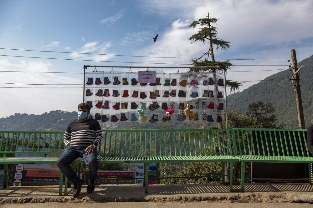 A man wearing a mask to protect himself from the coronavirus sits next to a display of face masks outside his shop in Dharmsala India